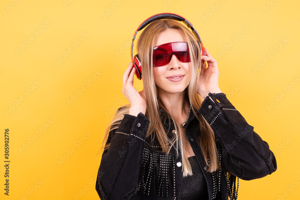 Beautiful young girl in red glasses and headphones on yellow background