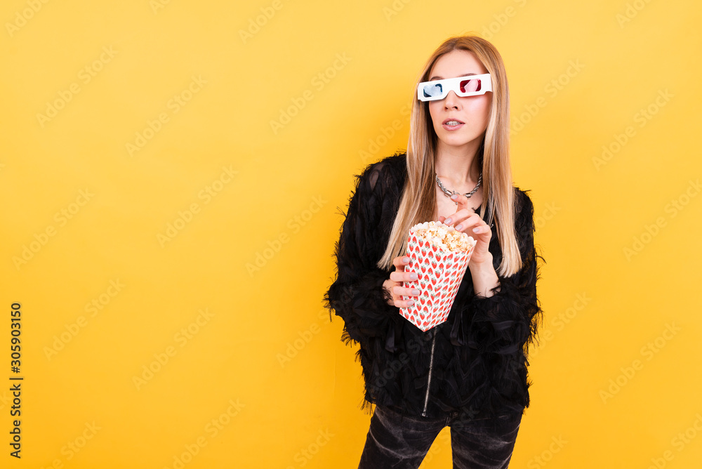 Beautiful young girl in 3d glasses holds bucket with popcorn on yellow background Beautiful young girl in 3d glasses holds bucket with popcorn on yellow background