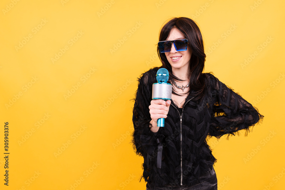 Obraz premium Beautiful young woman in glasses and with microphone on yellow background