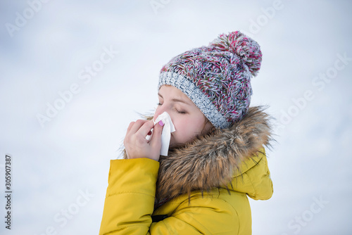 a girl with handkerchief outdoor in snow cold park in hat and coat. Woman blows her nose in winter