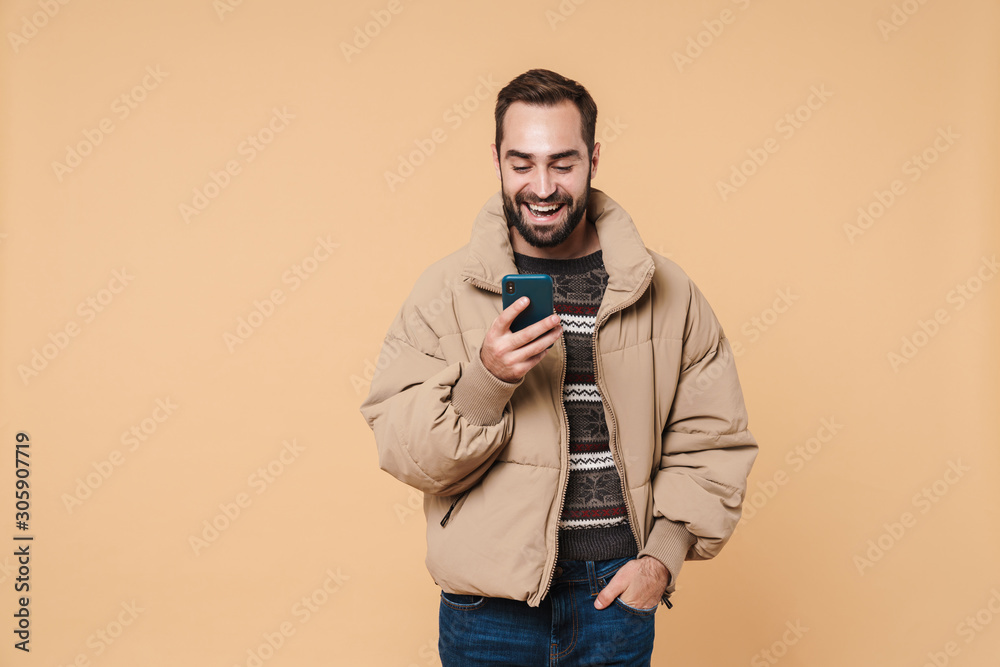 Image of attractive man in winter jacket smiling and holding smartphone Image of attractive man in winter jacket smiling and holding smartphone