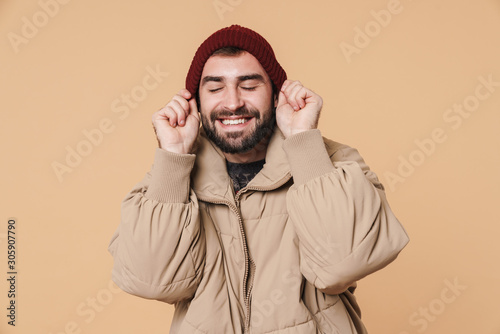 Image of cheerful man in winter jacket smiling and putting on his hat