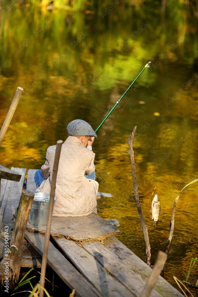 Kid fishing in a river, sitting on a wood pontoon Kid fishing in a river, sitting on a wood pontoon