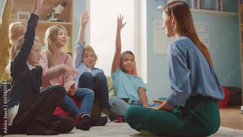 Elementary School Creativity Class: Children Sitting on the Carpet while Teacher Explains Lesson and Asks Question, Every Child Raises Hand with Answer. Learning in Modern Environment. Slow Motion