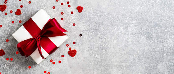 Valentines Day banner. White gift box with red ribbon on stone background decorated heart shaped confetti. Flat lay, top view. Love and romance concept.