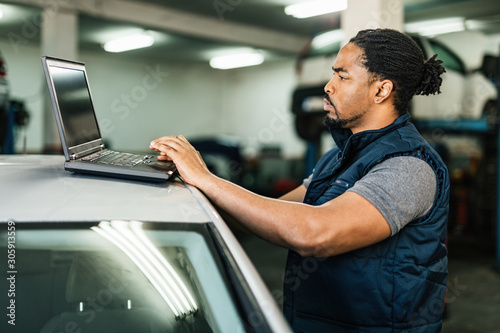 Young black mechanic using computer in auto repair shop.