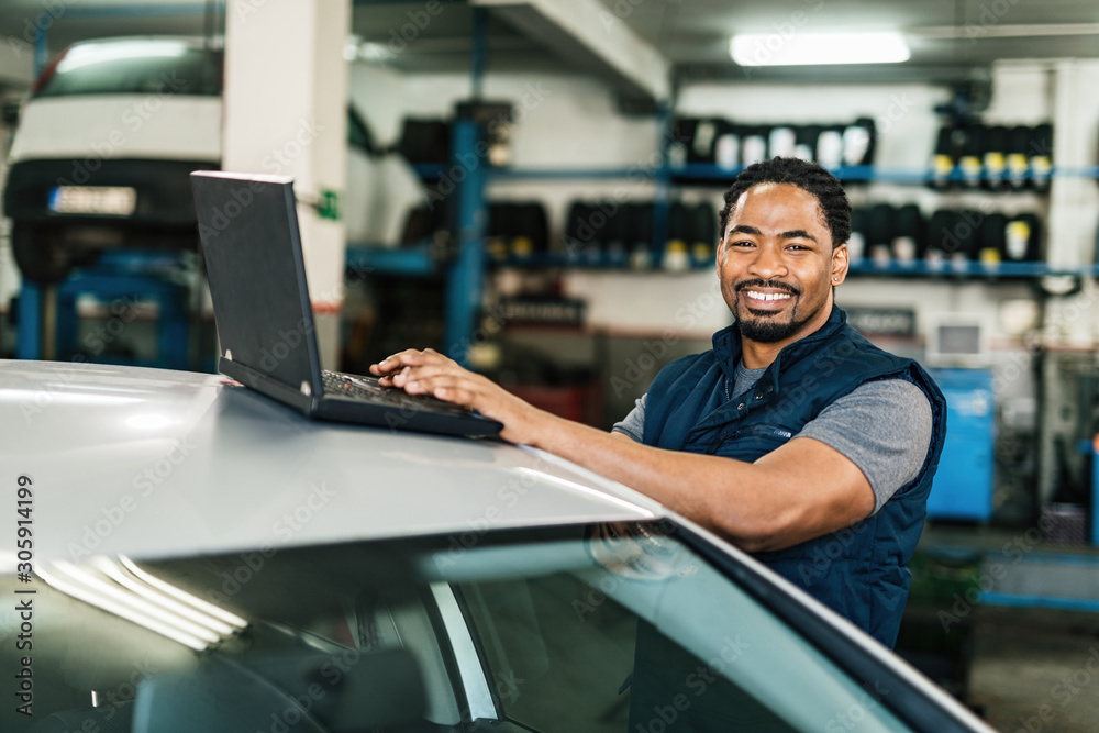 Happy African American car mechanic using laptop and looking at camera. Happy African American car mechanic using laptop and looking at camera.