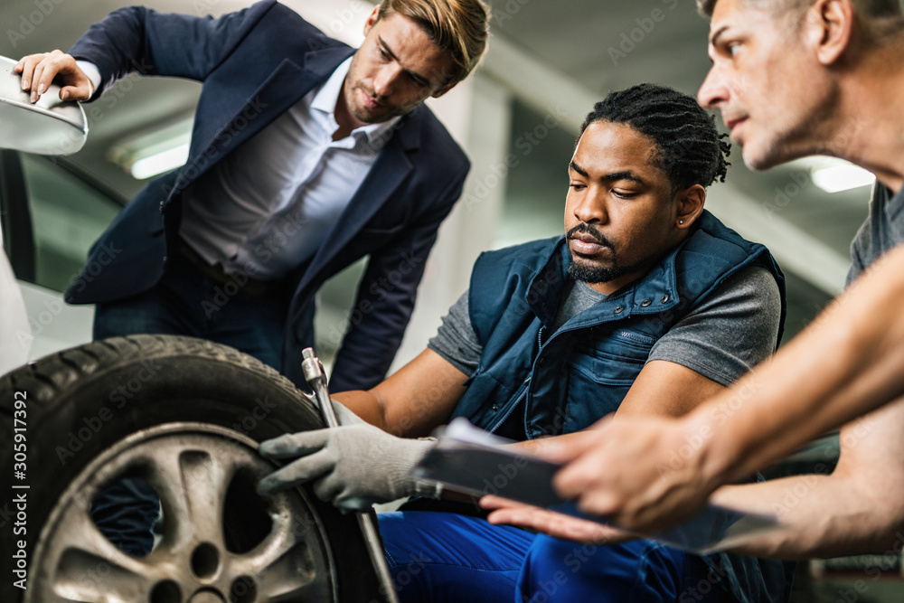 Fototapeta premium Auto mechanics repairing tire of customer's car at repair workshop.
