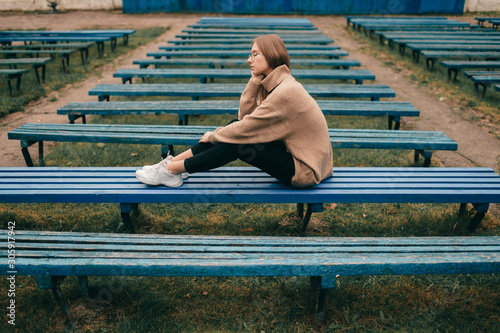 Portrait of lonelely sad girl siiting on bench in public place. photo