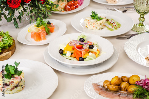 Served for holiday banquet restaurant table with Greek salad, dishes, snack, salads, cutlery, wine and water glasses. European food in a restaurant setting. Table set for an event party. catering