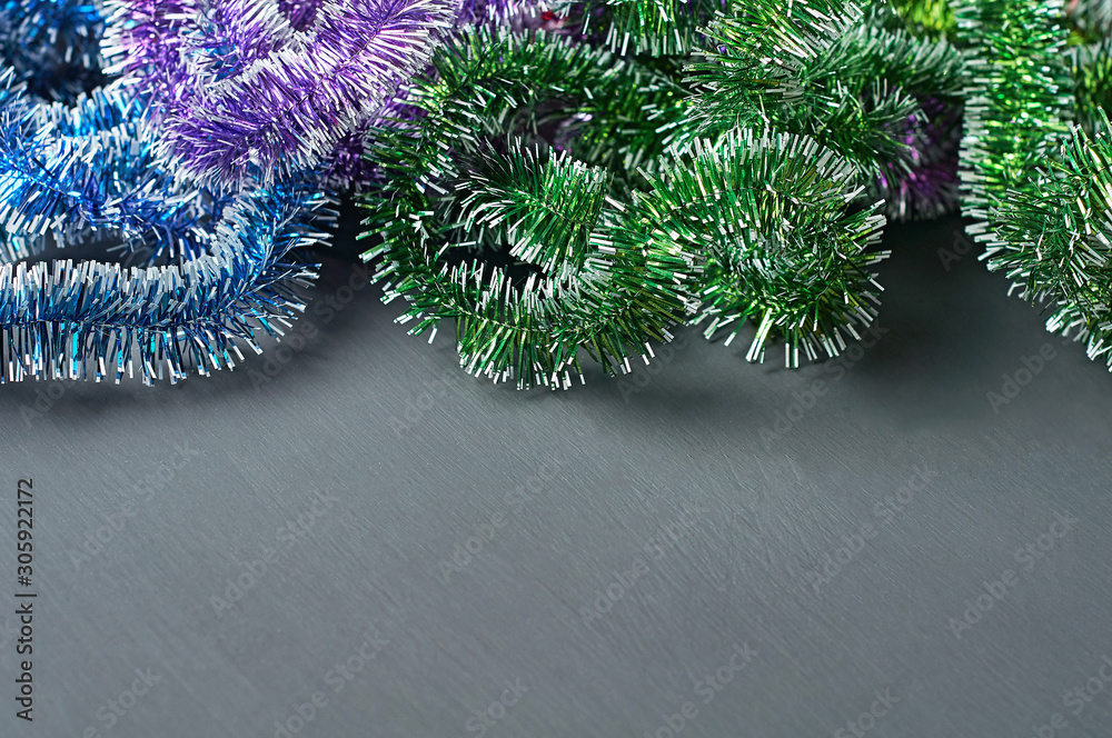 Scattered shiny festive tinsel of different color on dark concrete desk. Space for text Scattered shiny festive tinsel of different color on dark concrete desk. Space for text