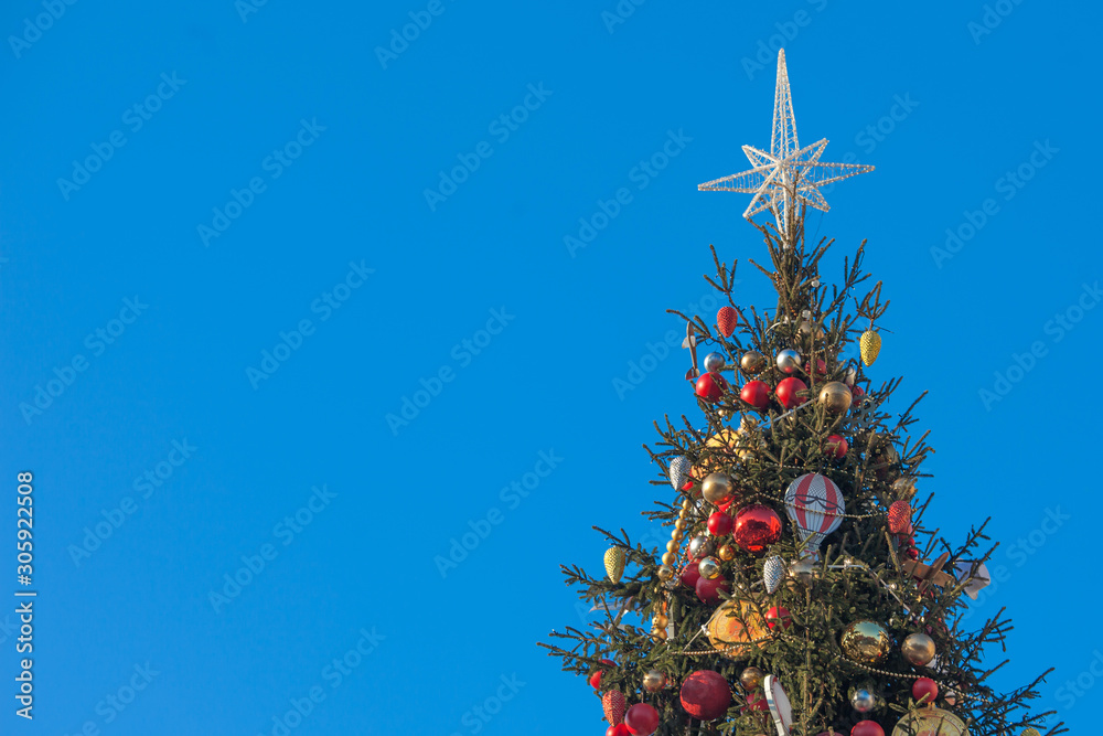 Decorated outdoor Christmas Tree with beautiful festive arrangement of fresh spruce with balls. Christmas morning with blue sky. Festive city street decor in winter holidays. Copy space