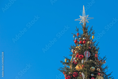 Decorated outdoor Christmas Tree with beautiful festive arrangement of fresh spruce with balls. Christmas morning with blue sky. Festive city street decor in winter holidays. Copy space