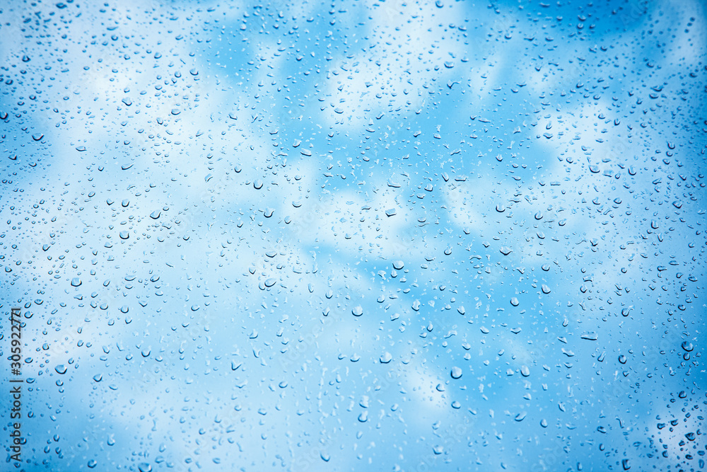 Natural pattern of raindrops on a window with a blue sky with clouds in the background. Textural background with wet drops of water on window.