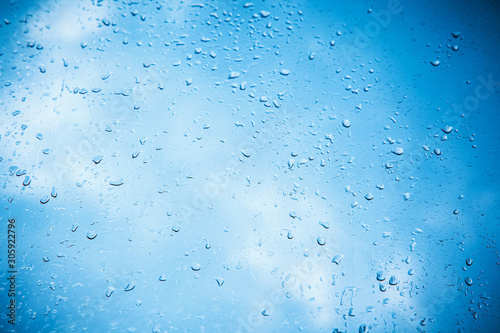Natural pattern of raindrops on a window with a blue sky with clouds in the background. Textural background with wet drops of water on window.