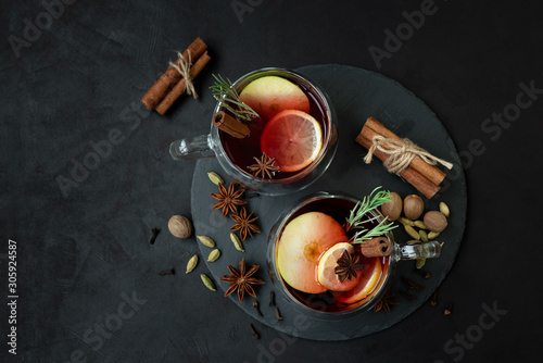 Two cups of Christmas mulled wine or punch with spices and lemon slices on dark wooden background. Christmas or New Year celebration concept