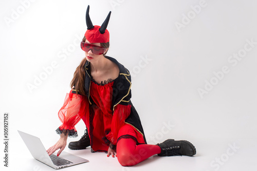 Sexy brunette woman in red tights, black boots and devil horns using laptop over white studio background. photo