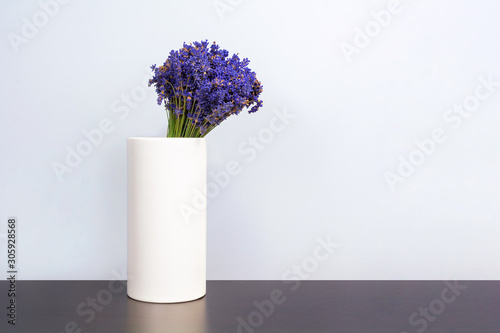Front view of Lavandula bouquet in minimalist white vase on dark table. The beautiful purple lavender flower  with white background and some space on the side