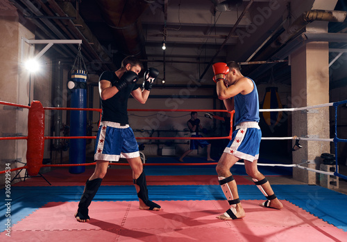 Young boxer practicing kickboxing with sparring partner in the ring at the sport club
