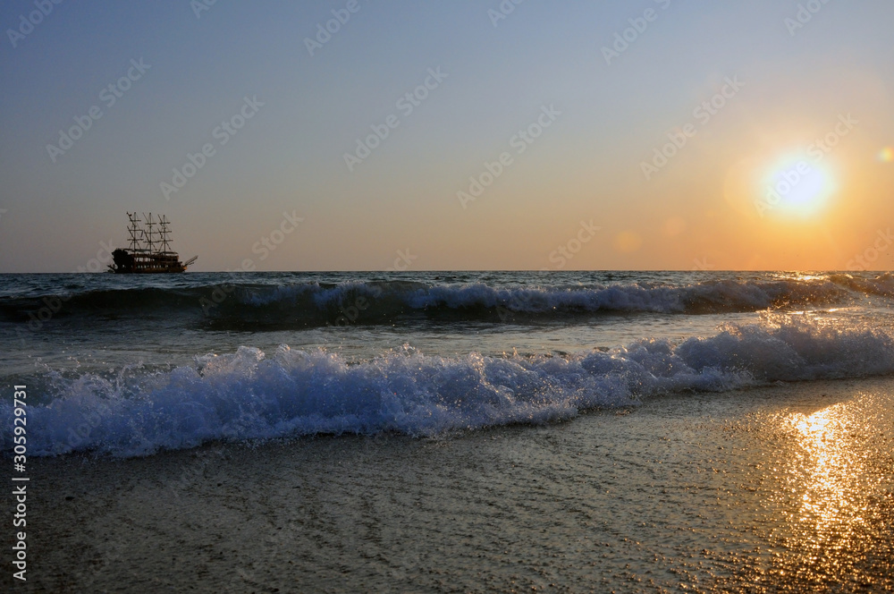 Tropical sunset background. Beautiful colorful ocean wave. Pleasure ship with masts on the horizon.