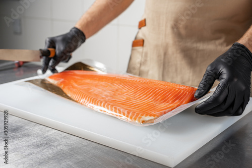 A man in black gloves unpacks a large salmon fillet.