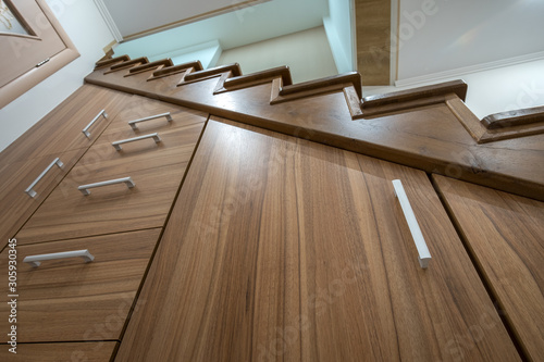 Modern architecture interior with luxury hallway with glossy wooden stairs in multi-storey house. Custom built pullout cabinets on glides in slots under stairs. Use of space for storage.