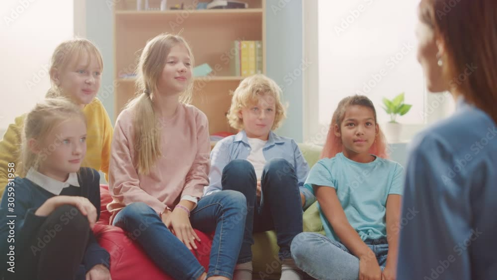 Elementary School Creativity Class: Children Sitting on the Bean Bags while Teacher Explains Lesson and Asks Question, Every Child Raises Hand with Answer. Learning in Modern Environment. Slow Motion
