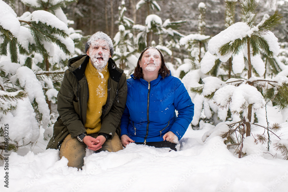 Portrait of funny couple with thier faces covered with snow standing on knnes in snowy forest