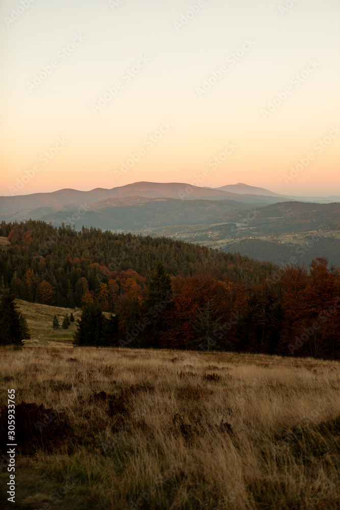 Majestic sunset in the mountains landscape. Sunset above hills and peaks, forest and yellow grass meadows.