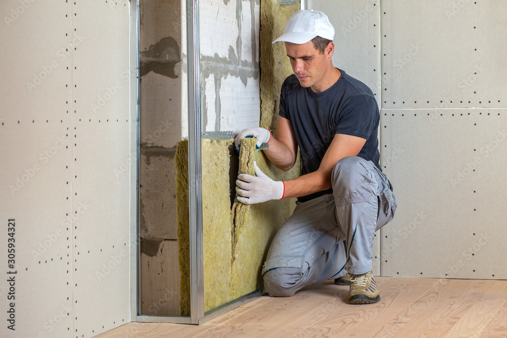 Worker insulating a room wall with mineral rock wool thermal insulation. Worker insulating a room wall with mineral rock wool thermal insulation.