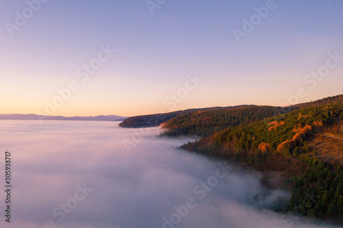Amazing aerial view of foggy and colorful forest on sunrise. Autumn landscape. Drone shot