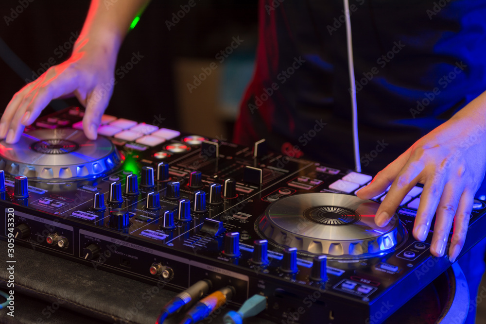 Naklejka premium Sound engineer on mixer, close up of DJ hands on stage mixing, disc jockey and mix tracks on sound mixer controller, playing music at bar, disco tech or night club party. 