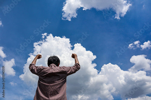 A man looking into the blue sky with white cloud holding arms up