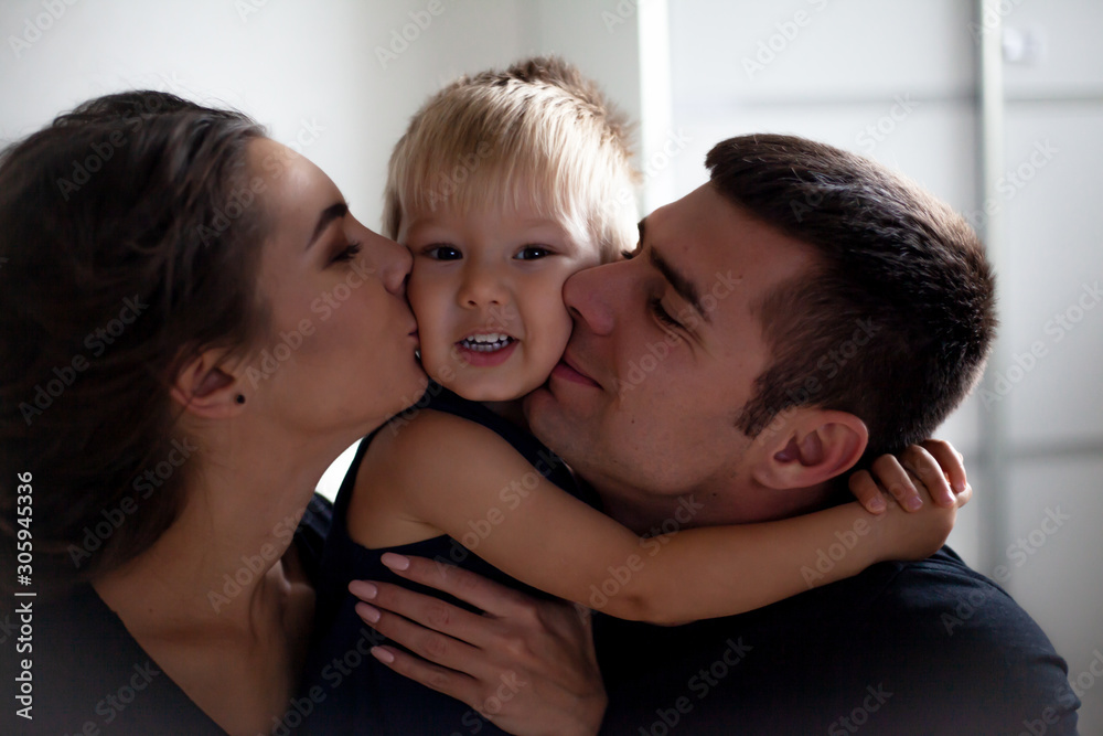 The caucasian family hugging in the home bedroom and kissing the baby. People dressed black clothes, pajamas The caucasian family hugging in the home bedroom and kissing the baby. People dressed black clothes, pajamas