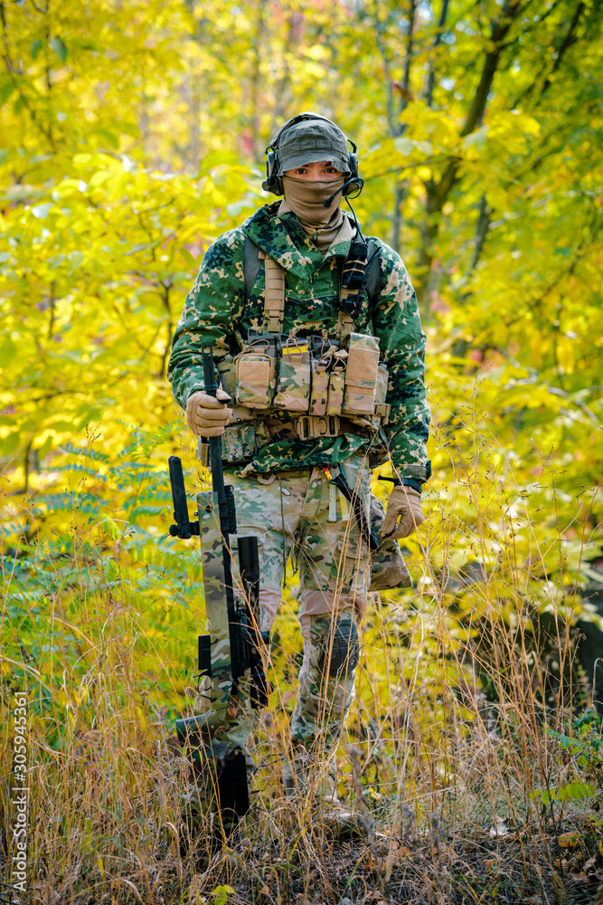 Airsoft, man in uniform stand with sniper rifle on autmn forest background