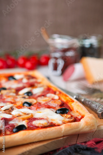 Homemade rectangular pizza on a rustic table with ingredients