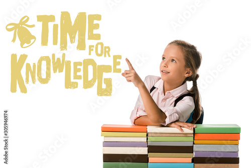 positive schoolkid pointing with finger at time for knowledge letters near colorful books on white