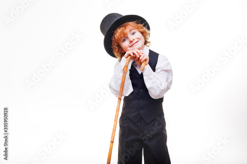 kid actor in the theatre, stylish boy in hat isolated on white background, happy child actor with a cane in his hand dressed in a black suit, talented red curly boy playing in the theatre