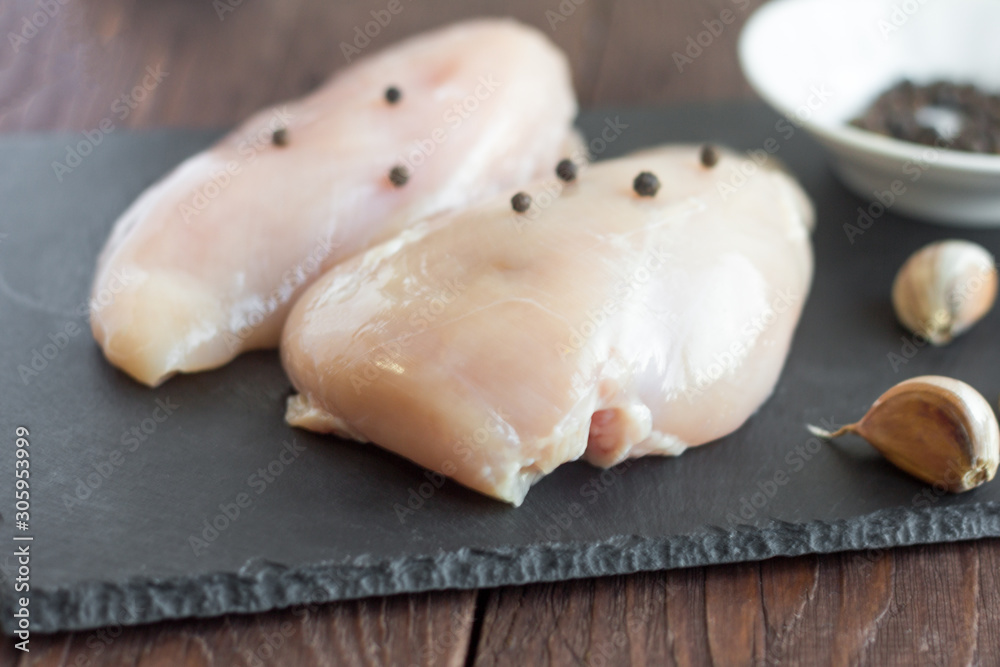 Raw chicken fillet on a stone Board with pepper and garlic.Cooking Raw chicken fillet on a stone Board with pepper and garlic.Cooking