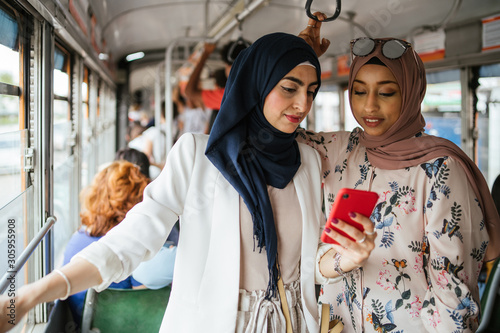 Arab italian friends on the tram in Italy - Millennials women talking during the trip to the city while look the smartphone photo