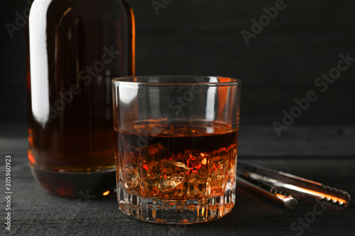 Bottle and glass of whiskey on wooden background, space for text