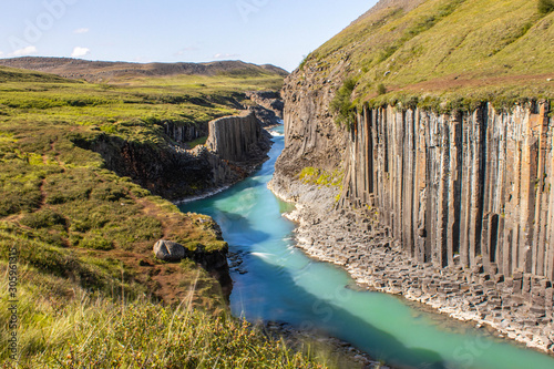 Recessed clear cyan river in grass mountains, canyun with basalt columns in Iceland, Studlagil Canyon