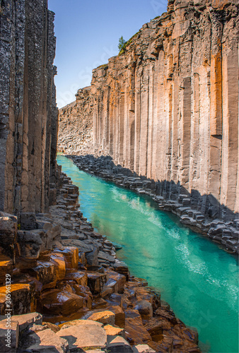 Clear turquoise and cyan river flowing through high basalt colmun canyon in Iceland, Studlagil Canyon