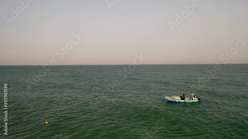 Aerial backward fly reveal two man on a small fish boat a lone in the sea, drone shot photo