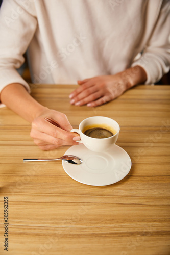 cropped view of woman holding cup with hot coffee in cafe