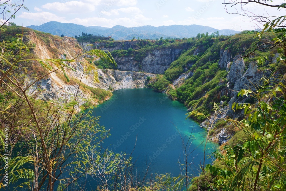 Fototapeta premium Beautiful scenic of a mining quarry with a waterlogging area in the middle against the mountain and blue sky background which is a tourist attraction in Chon Buri, Thailand