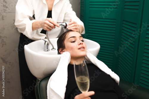 Young girl relaxes in a beauty salon with a glass of champagne while washing hair