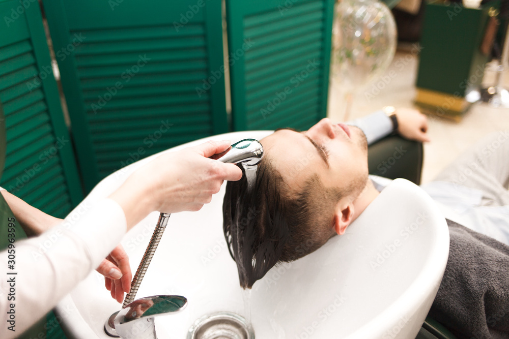 Hairdresser washes a client’s hair before cutting. Serious handsome man washes his head in a beauty salon Hairdresser washes a client’s hair before cutting. Serious handsome man washes his head in a beauty salon