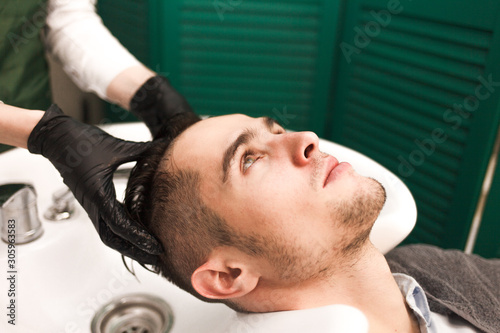 Hairdresser washes a client’s hair before cutting. Serious handsome man washes his head in a beauty salon