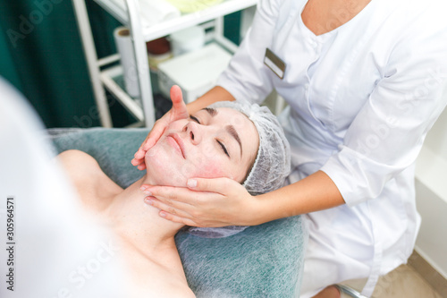 Doctor beautician makes cosmetic facial massage. Woman relaxes on a cosmetic chair